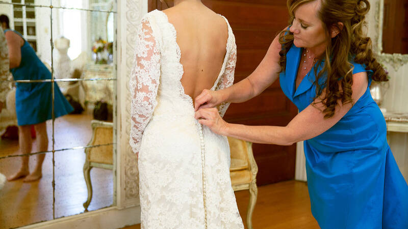 mother buttoning up the back of bride's gown
